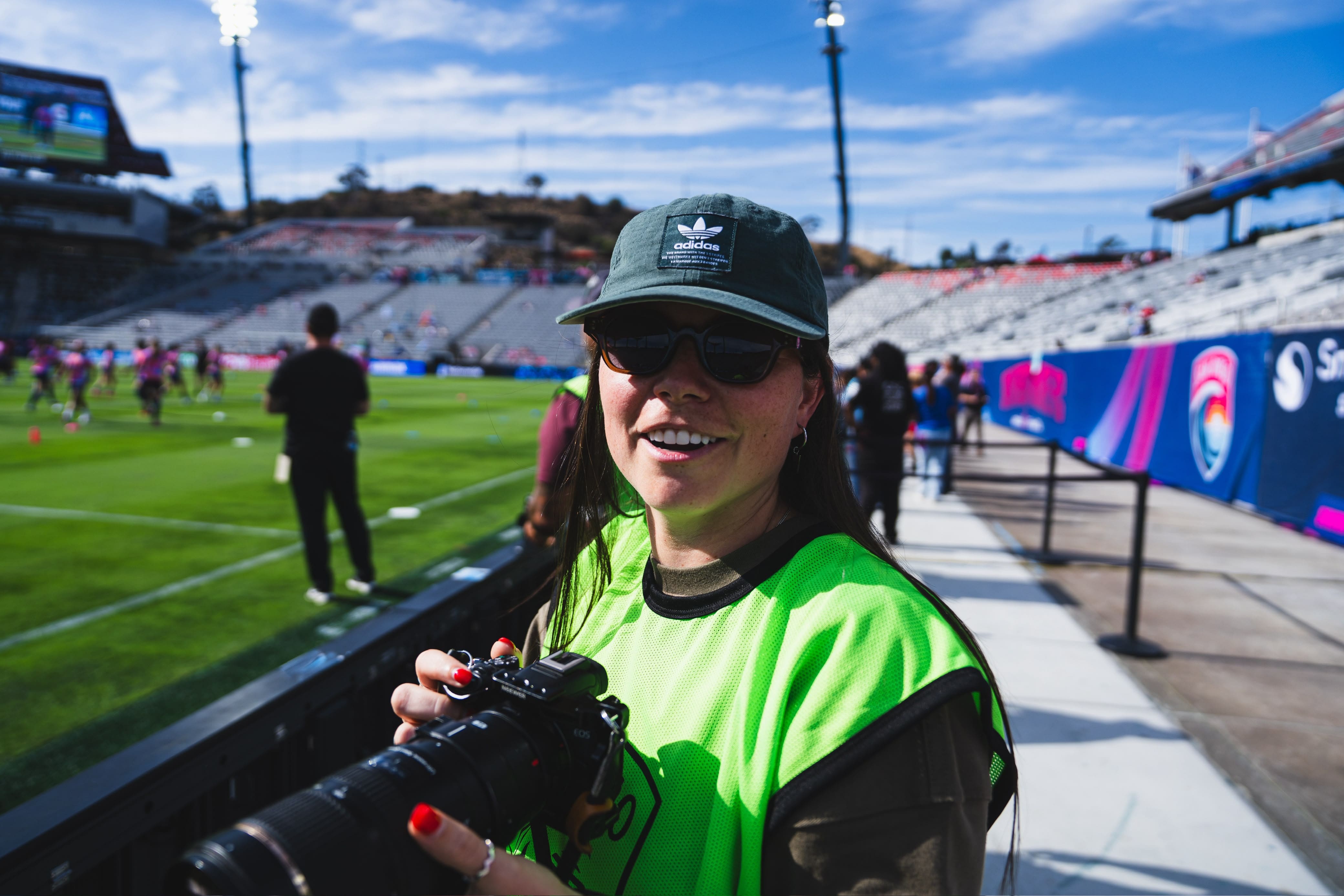 Stephanie DeMello holding a professional camera on the sidelines of a soccer game